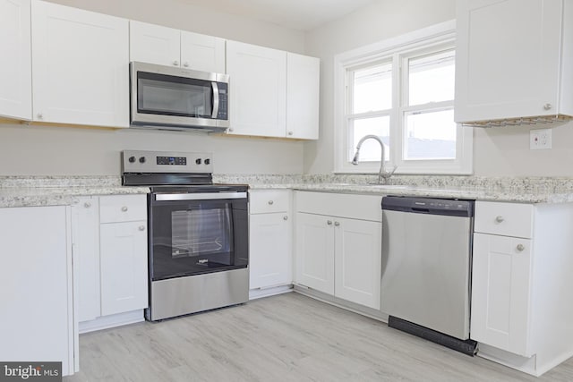 kitchen with light wood finished floors, appliances with stainless steel finishes, a sink, and white cabinetry