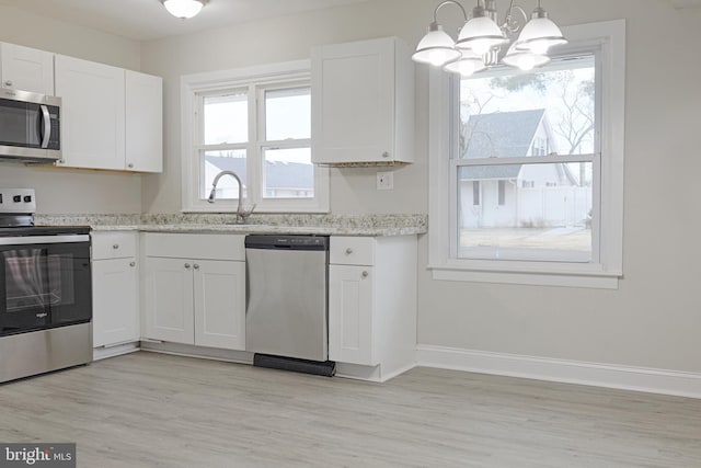 kitchen featuring light wood-style flooring, appliances with stainless steel finishes, white cabinets, light stone countertops, and baseboards