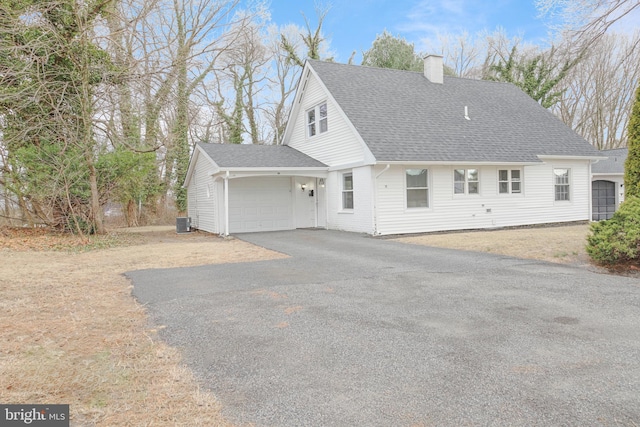 view of front facade featuring a chimney, central air condition unit, a shingled roof, a garage, and driveway