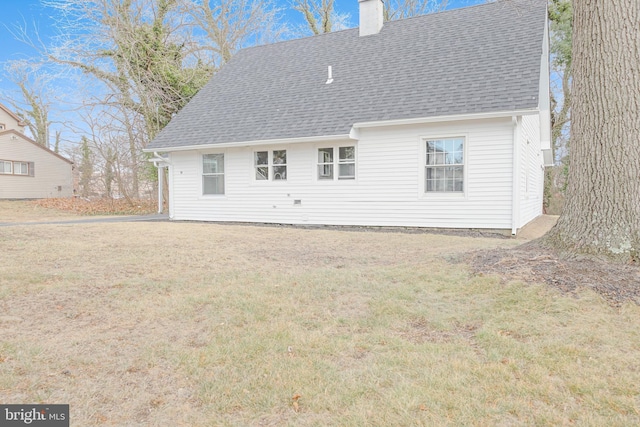 back of property featuring roof with shingles, a lawn, and a chimney