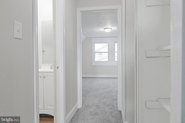 hallway featuring carpet, a sink, and baseboards