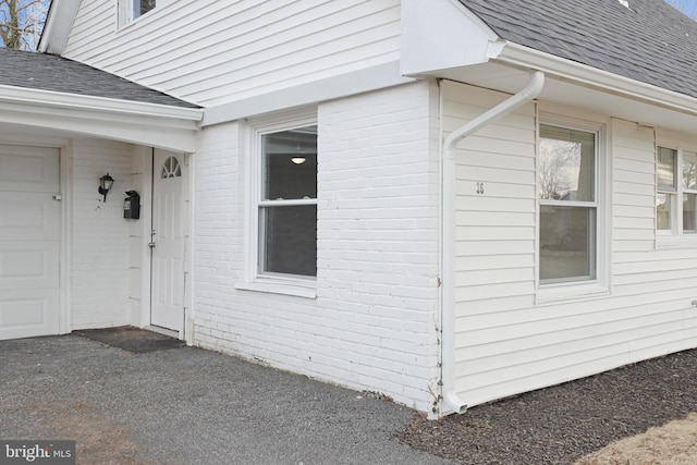 doorway to property with a shingled roof and brick siding