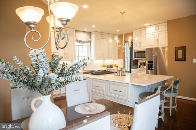 kitchen with a kitchen island, an inviting chandelier, stainless steel appliances, decorative backsplash, and light countertops