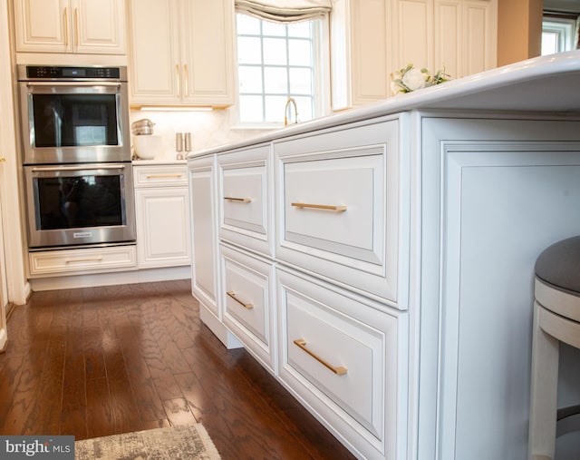 kitchen with double oven, dark wood-type flooring, light countertops, and white cabinetry