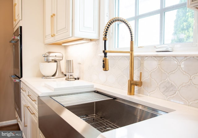 interior details featuring oven, a sink, baseboards, light countertops, and tasteful backsplash