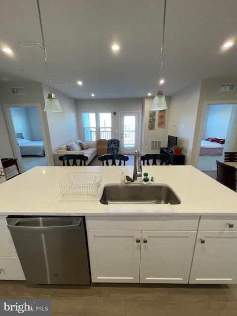 kitchen featuring visible vents, dishwasher, open floor plan, white cabinetry, and a sink