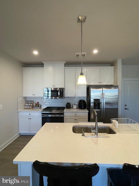 kitchen featuring a breakfast bar area, a sink, stainless steel appliances, light countertops, and backsplash