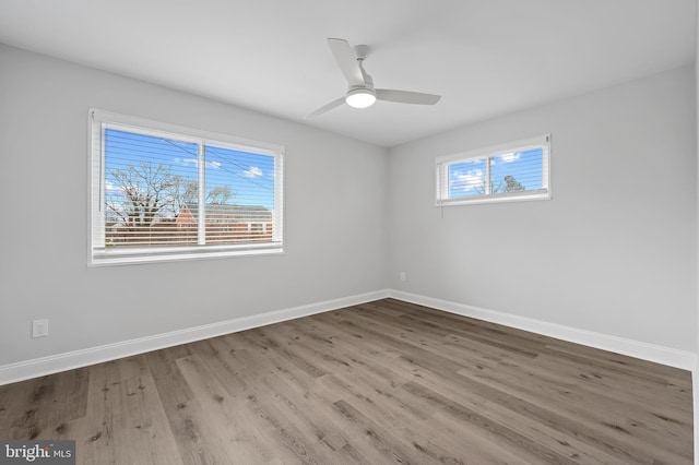 unfurnished room featuring a ceiling fan, wood finished floors, a wealth of natural light, and baseboards