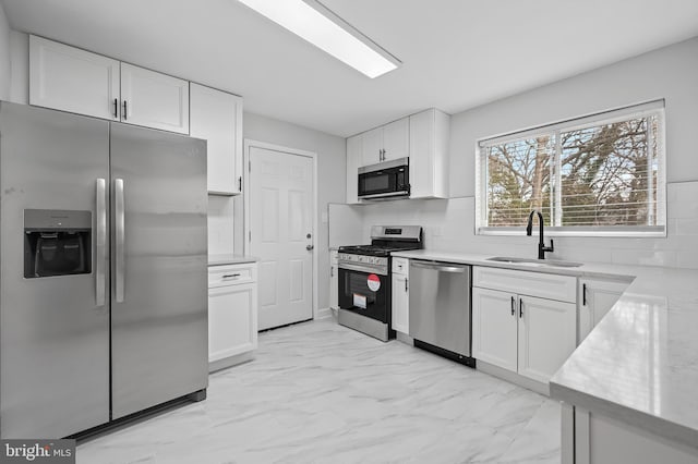 kitchen with appliances with stainless steel finishes, marble finish floor, white cabinetry, and a sink