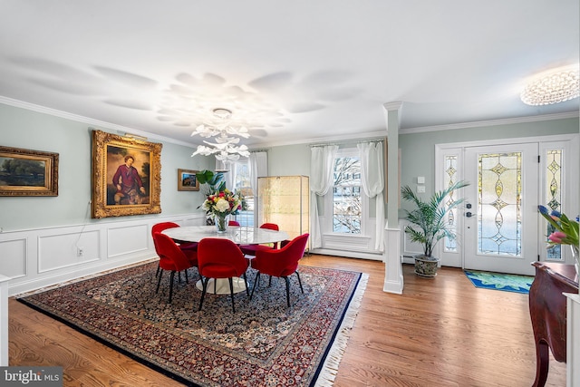 dining space with crown molding, light wood-style floors, a wainscoted wall, and a notable chandelier