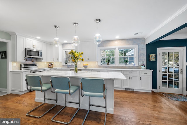 kitchen with tasteful backsplash, appliances with stainless steel finishes, ornamental molding, white cabinets, and wood finished floors