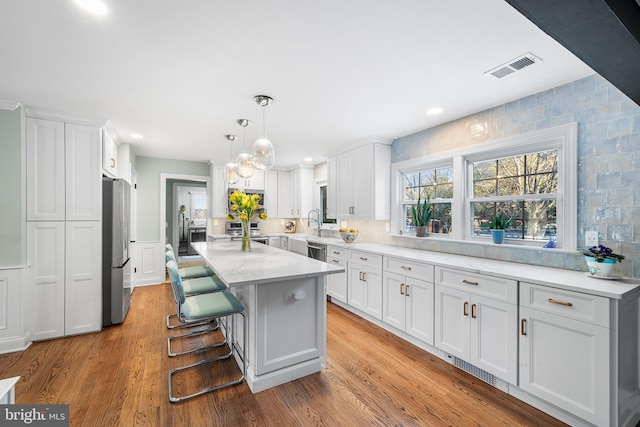 kitchen with a center island, stainless steel appliances, visible vents, white cabinetry, and wood finished floors