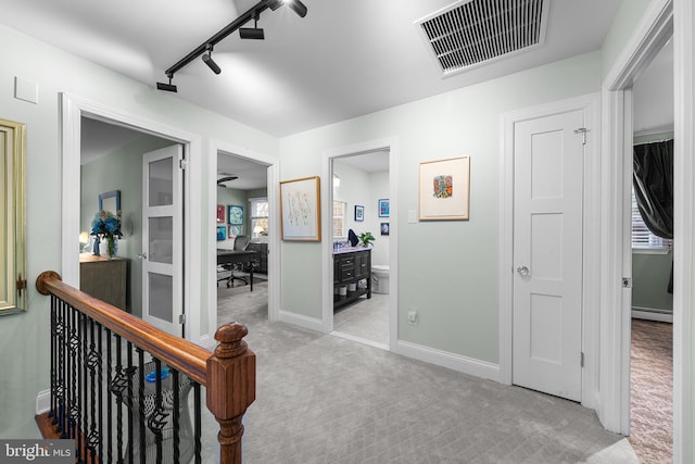 hallway with carpet floors, visible vents, baseboards, baseboard heating, and rail lighting