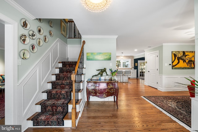 entryway featuring a wainscoted wall, stairway, ornamental molding, wood finished floors, and a decorative wall