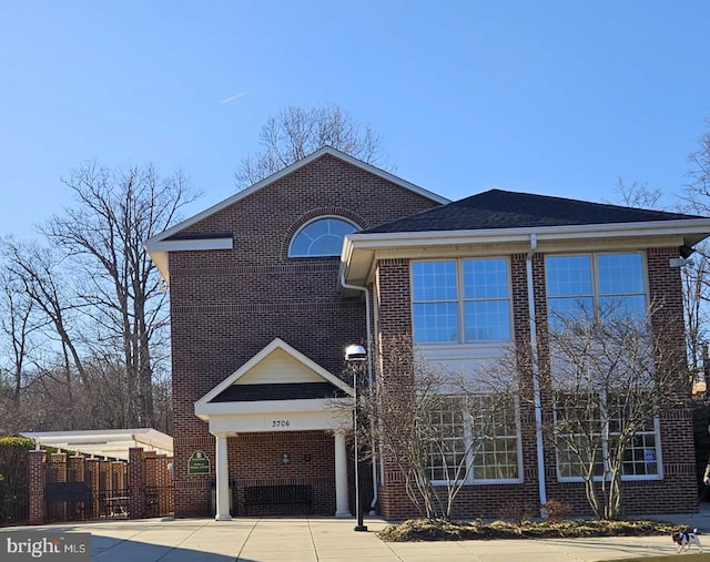 traditional-style house featuring roof with shingles and brick siding