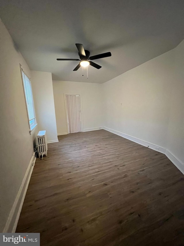 empty room with dark wood-style floors, ceiling fan, baseboards, and radiator