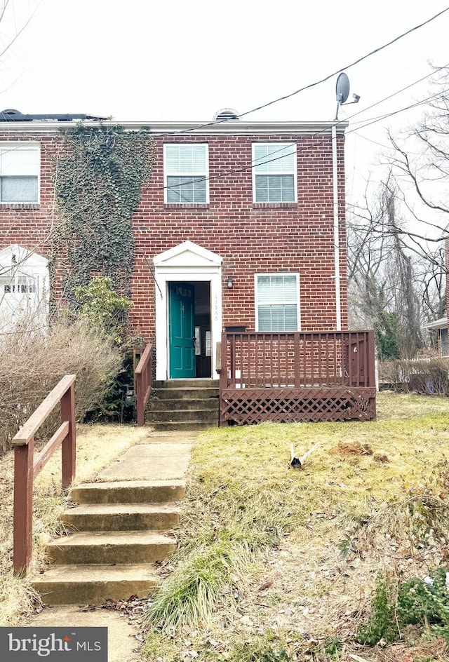 view of front facade with brick siding, a deck, and a front lawn