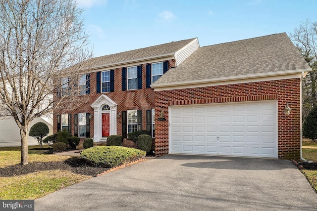 colonial-style house featuring brick siding, aphalt driveway, a garage, and roof with shingles