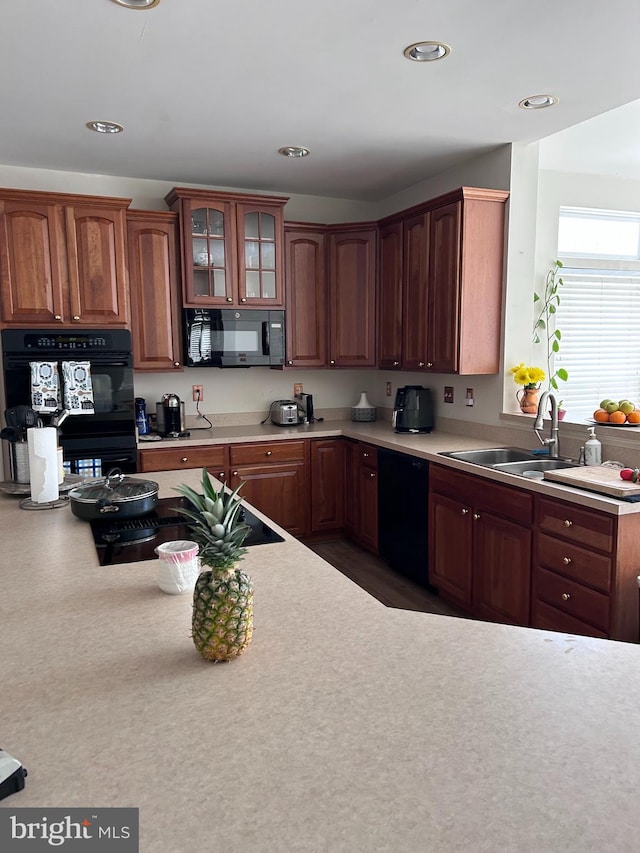 kitchen with glass insert cabinets, black appliances, light countertops, and a sink