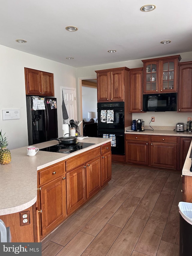 kitchen featuring light wood-type flooring, black appliances, recessed lighting, light countertops, and glass insert cabinets