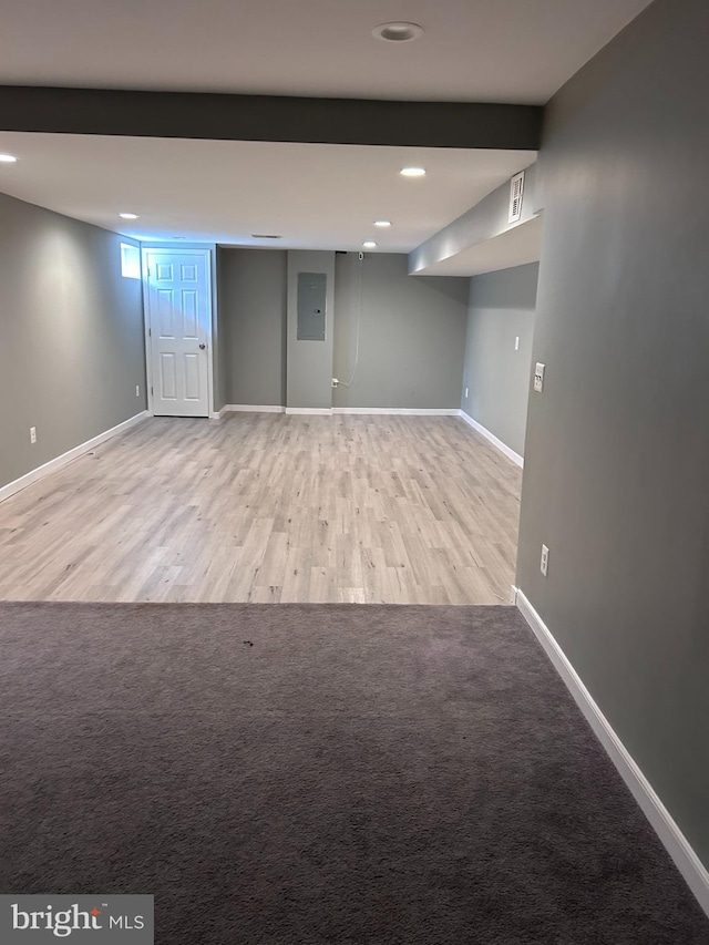 below grade area with electric panel, visible vents, baseboards, and wood finished floors