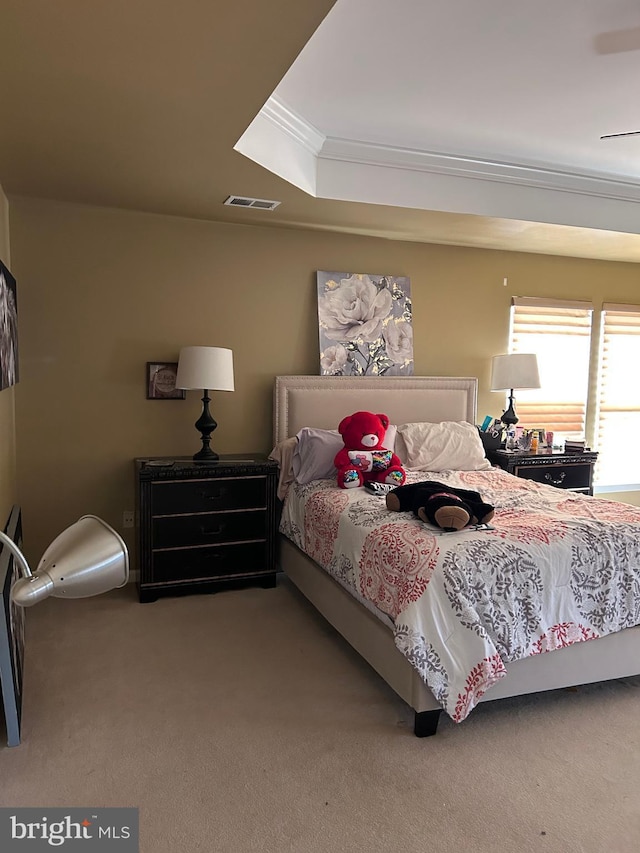 bedroom with a tray ceiling, visible vents, ornamental molding, and carpet flooring