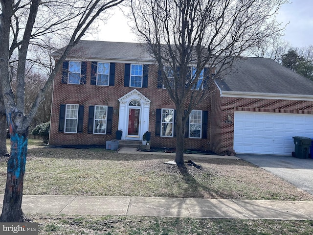 colonial house with an attached garage, brick siding, and driveway