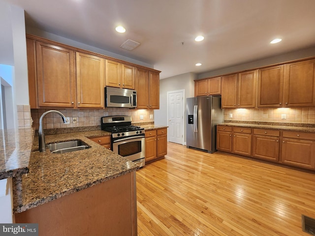 kitchen with stainless steel appliances, a sink, visible vents, light wood-type flooring, and brown cabinets