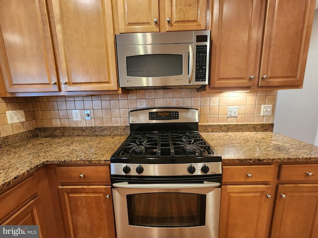 kitchen with tasteful backsplash, appliances with stainless steel finishes, brown cabinets, and light stone counters