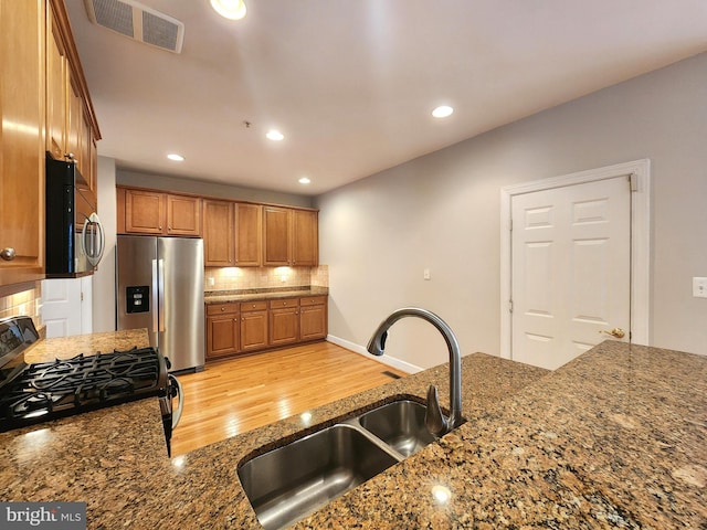 kitchen featuring visible vents, brown cabinetry, decorative backsplash, appliances with stainless steel finishes, and a sink