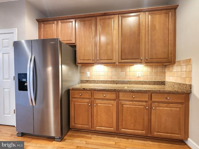 kitchen with light wood-type flooring, brown cabinets, and stainless steel refrigerator with ice dispenser