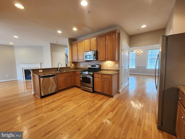 kitchen featuring a fireplace, a sink, appliances with stainless steel finishes, brown cabinets, and tasteful backsplash