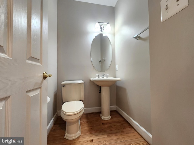 half bath with toilet, baseboards, and wood finished floors