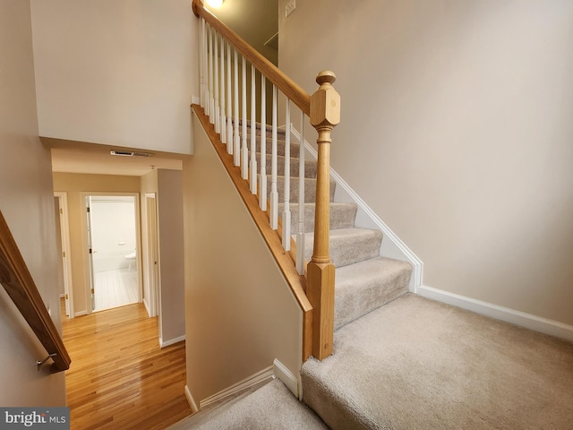 staircase featuring carpet floors, wood finished floors, visible vents, and baseboards