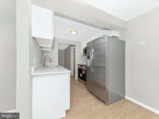 kitchen featuring light wood finished floors, white cabinets, appliances with stainless steel finishes, light countertops, and a sink