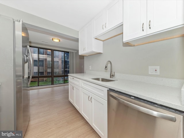 kitchen featuring appliances with stainless steel finishes, white cabinetry, a sink, and light wood finished floors