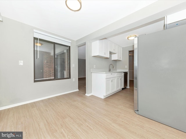 kitchen featuring light countertops, light wood-style floors, freestanding refrigerator, white cabinetry, and baseboards