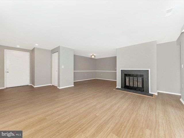 unfurnished living room with light wood-type flooring, a glass covered fireplace, and baseboards