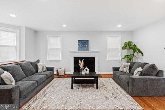 living room featuring baseboards, wood finished floors, a fireplace with flush hearth, and recessed lighting