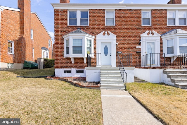 view of front of home with brick siding, a chimney, and a front yard