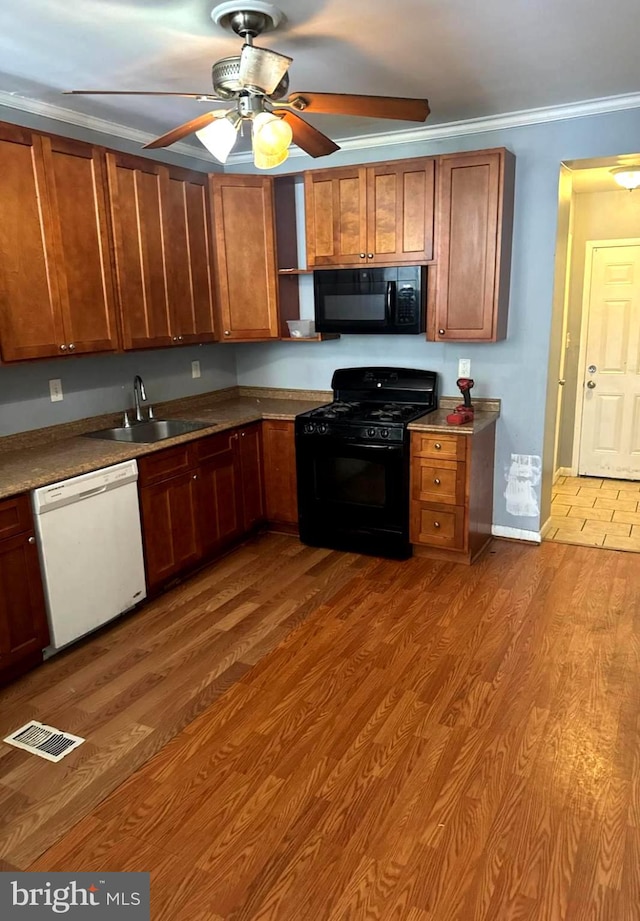 kitchen featuring wood finished floors, a sink, visible vents, ornamental molding, and black appliances