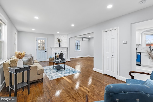 living room with a large fireplace, baseboards, wood finished floors, a wall mounted AC, and recessed lighting