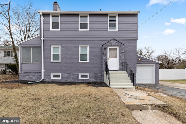 view of front of home featuring aphalt driveway, brick siding, a chimney, fence, and a front lawn