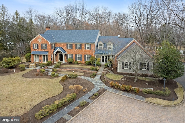 colonial house featuring brick siding, a chimney, and a front yard