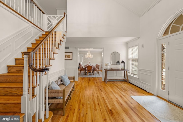 entrance foyer with light wood-style flooring, ornamental molding, stairs, a chandelier, and a decorative wall