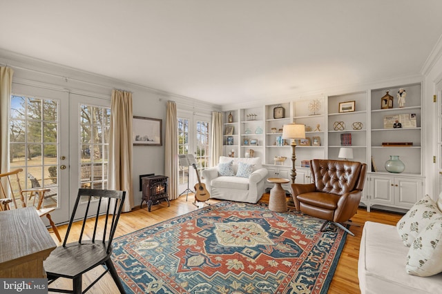 living area with light wood-type flooring, french doors, crown molding, and a wood stove