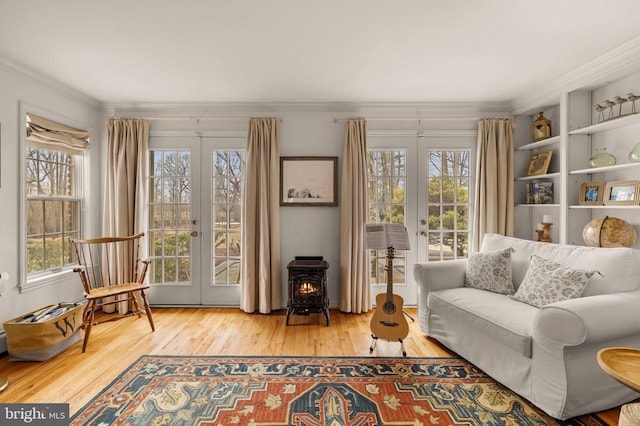 living area featuring french doors, wood finished floors, a wood stove, and crown molding