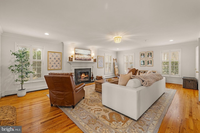 living area featuring ornamental molding, recessed lighting, a glass covered fireplace, and light wood-style floors