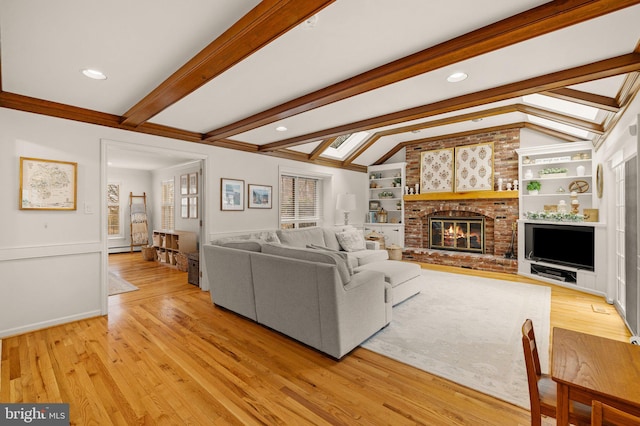 living area with vaulted ceiling with skylight, a brick fireplace, light wood-style flooring, and built in shelves