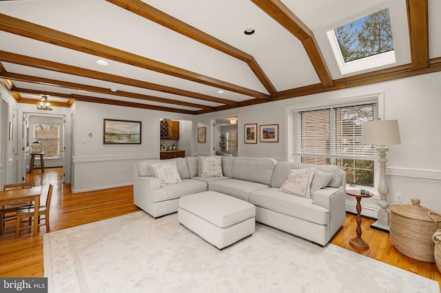 living room with a healthy amount of sunlight, lofted ceiling with beams, a baseboard heating unit, and wood finished floors